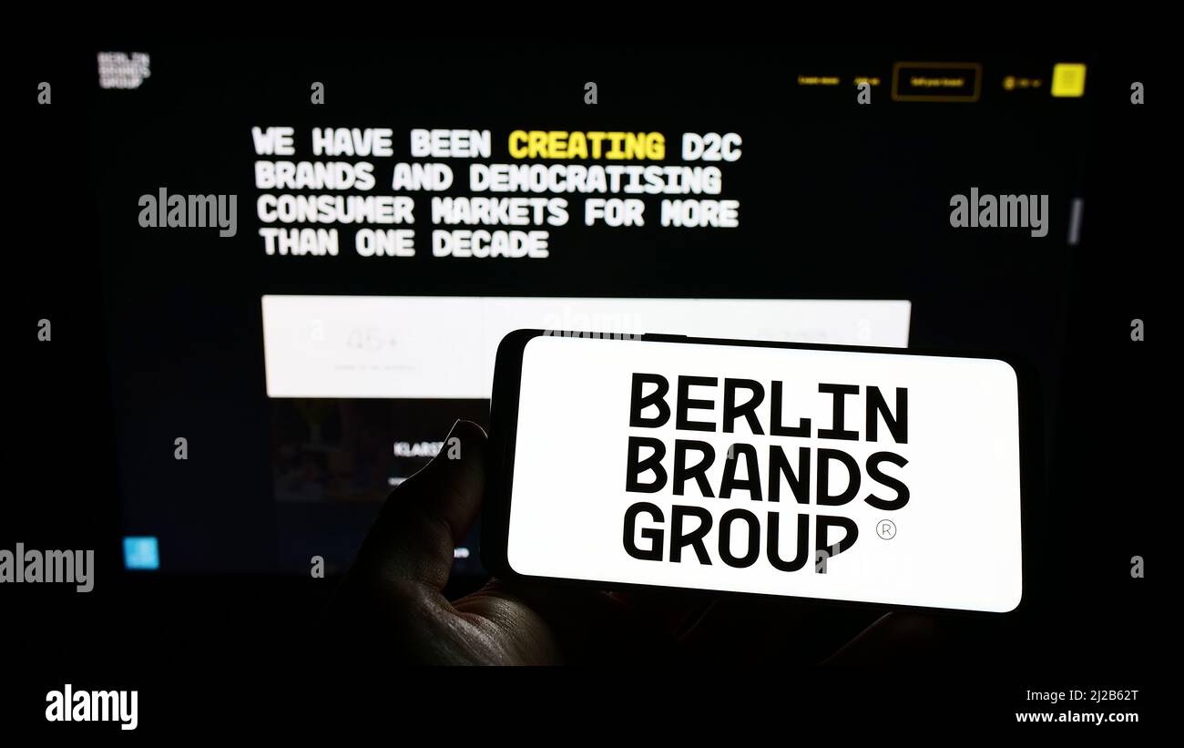 Person holding cellphone with logo of company Chal-Tec GmbH (Berlin Brands Group) on screen in front of business webpage. Focus on phone display. Stock Photo