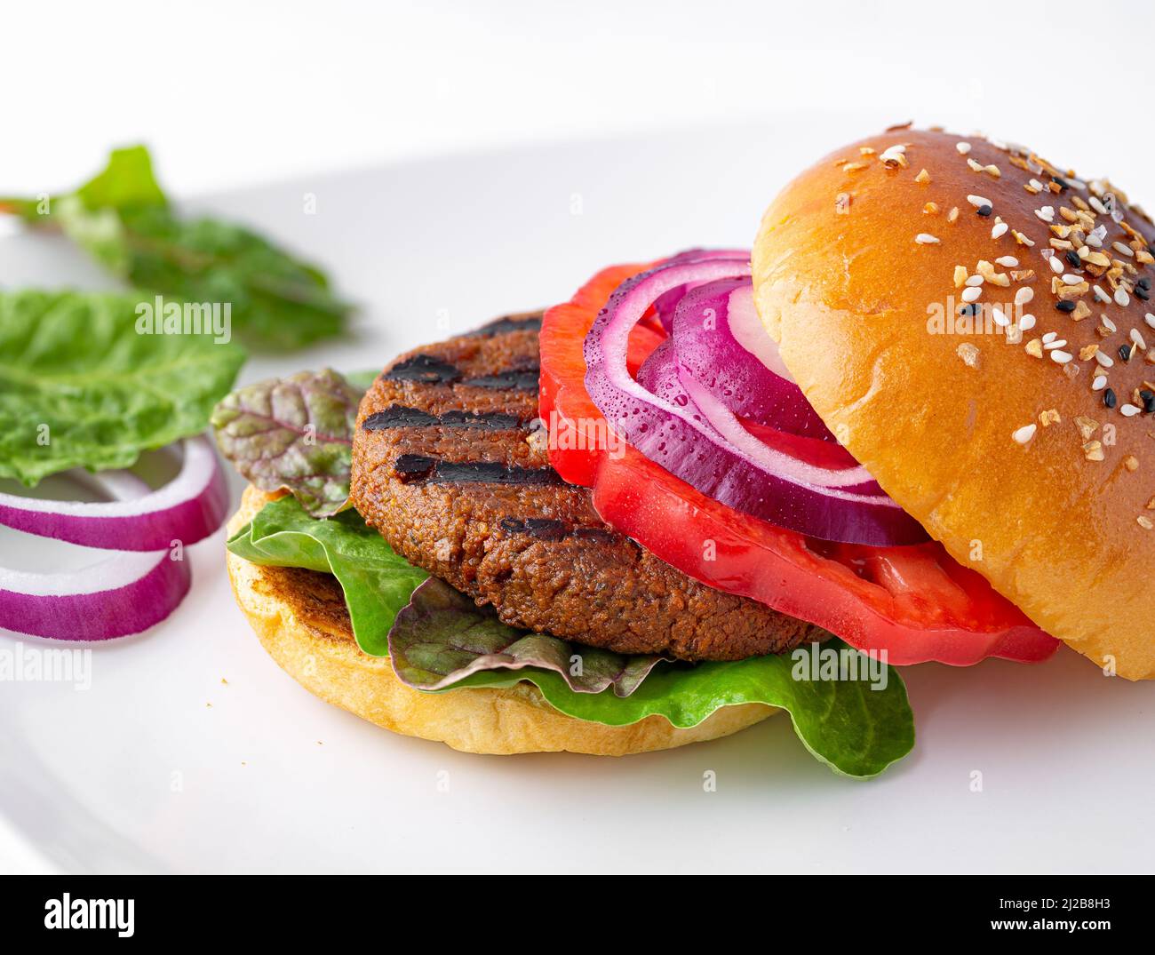 Plant based veggie burger with leafy greens, heirloom tomato, red onion, on a brioche bun topped with sesame seed and dried herb mix Stock Photo