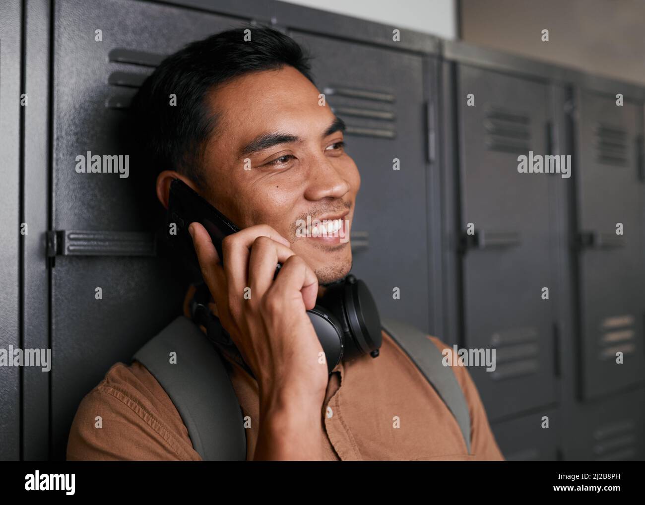 A young South East Asian man talks on the phone in front of campus lockers Stock Photo