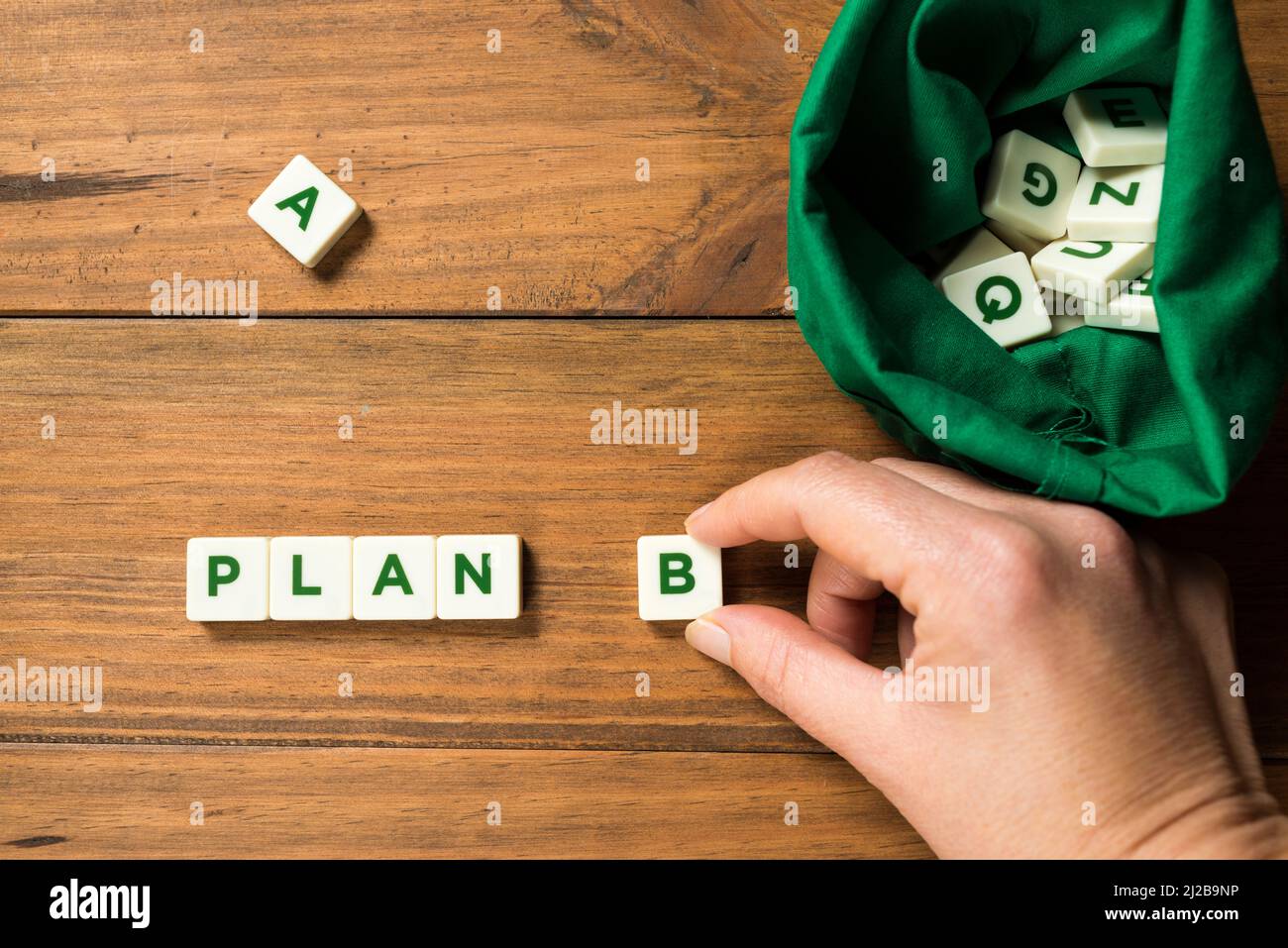A hand placing a piece with the letter B next to the word PLAN, next to a bag full of letters. A piece with the letter A appears displaced. Concept of Stock Photo