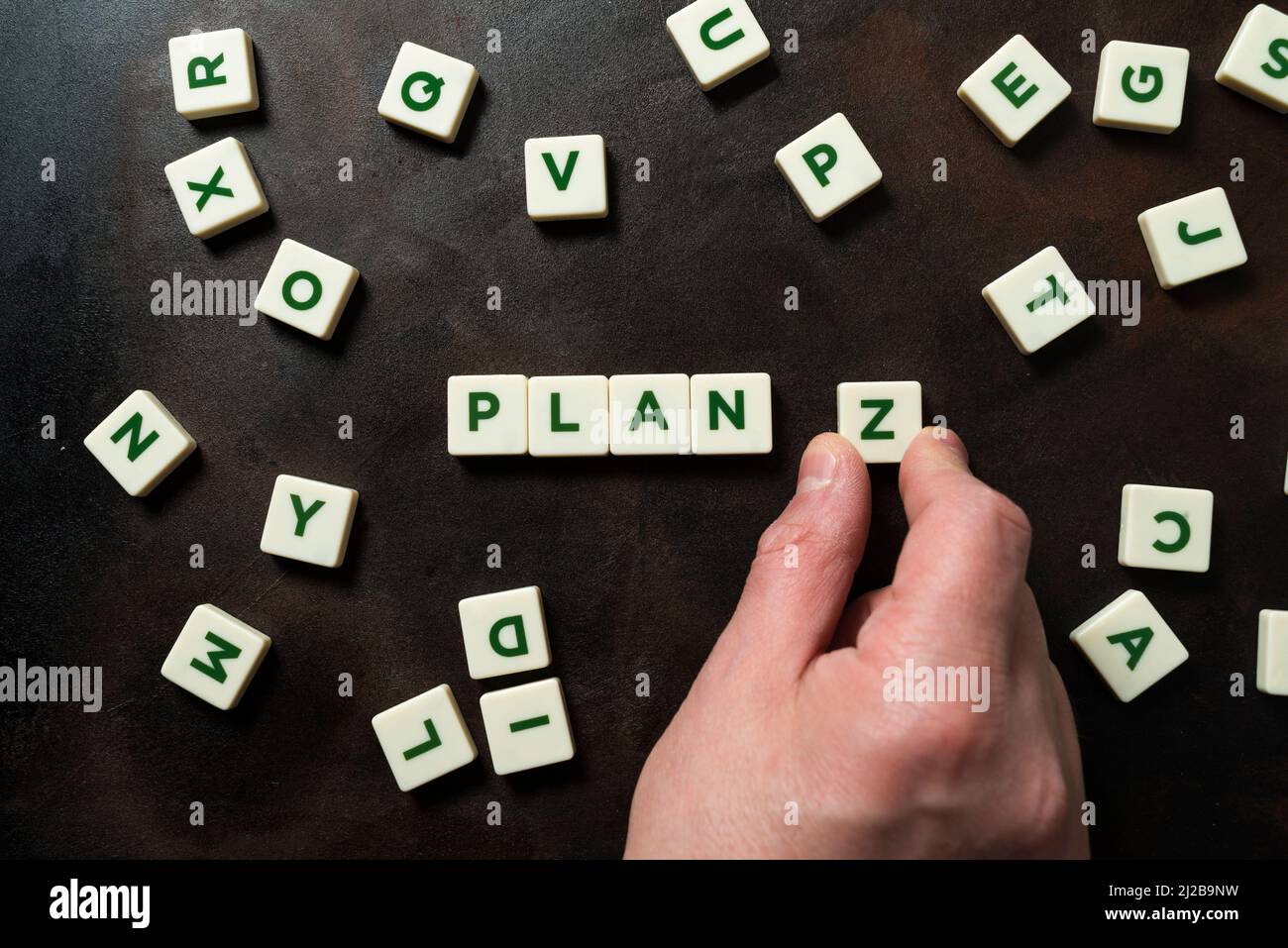 A hand places a piece with the letter Z next to the word PLAN, other pieces appear jumbled around it. Concept of planning for the future, resilience a Stock Photo