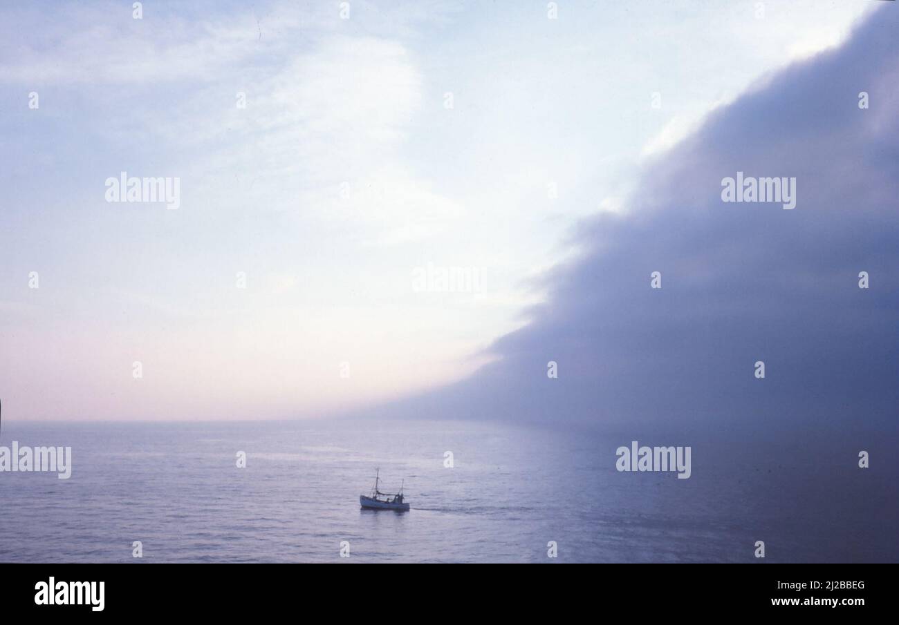 Fishing boat dominated by huge squall cloud at sea, Sep 1979 Stock Photo