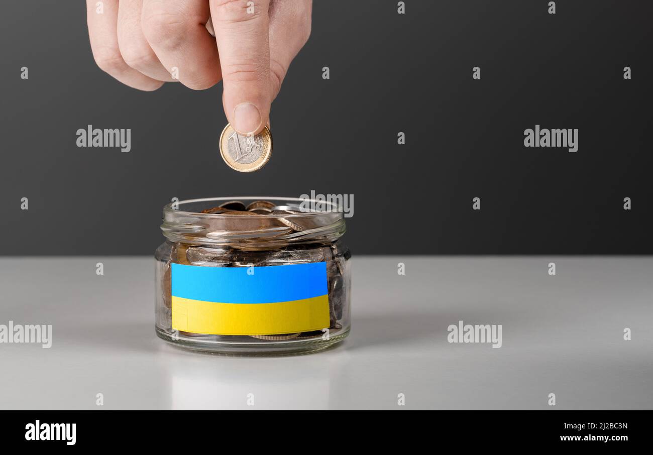 donation for ukrainian refugees. Help and financial assistance to Ukraine. donation jar with Ukrainian flag. Ukrainian war, donations, Hand putting Co Stock Photo