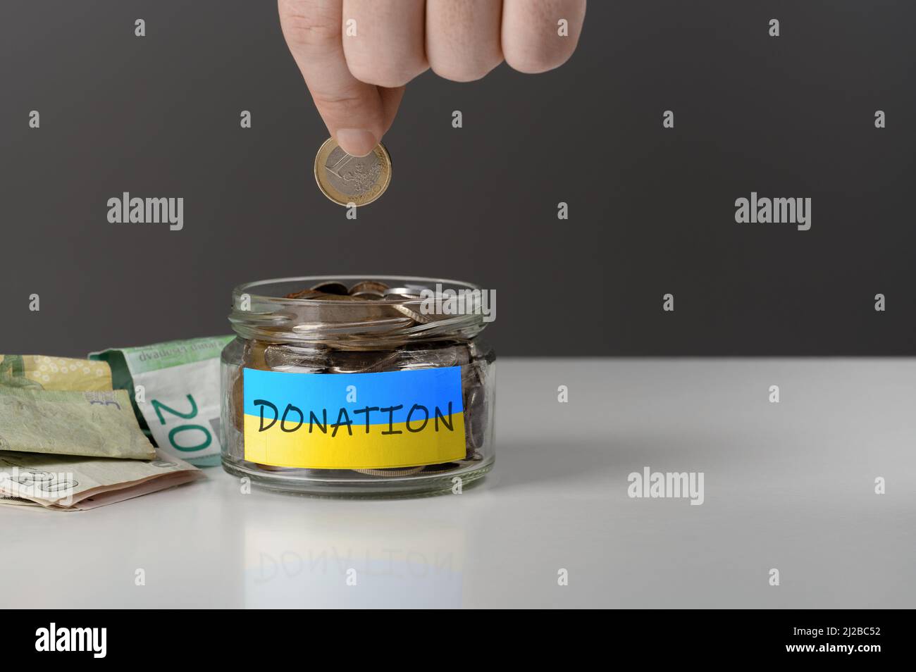 Donation for Ukraine concept. Help and financial assistance to Ukraine. donation jar with Ukrainian flag. Ukrainian war, donations, Hand putting Coins Stock Photo