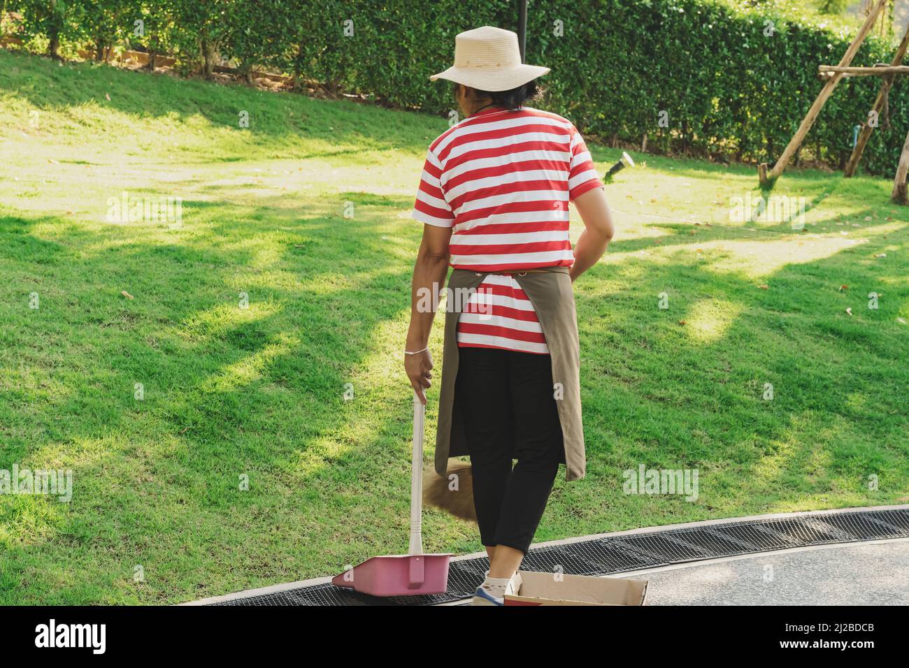 Female worker sweeping yard with broom tool and dustpan in ornamental