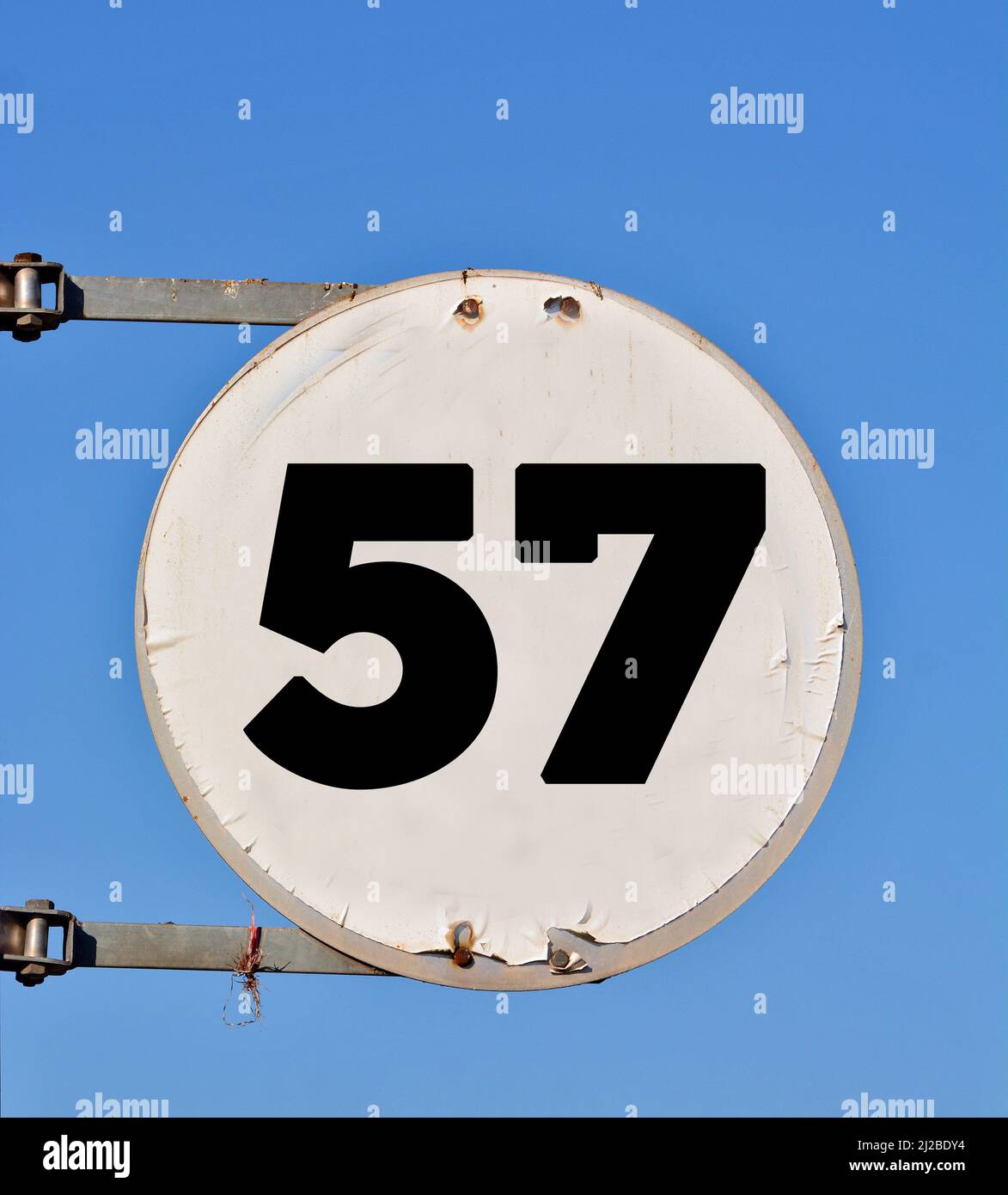 A speed limit sign with number 57 added on it against a blue sky 