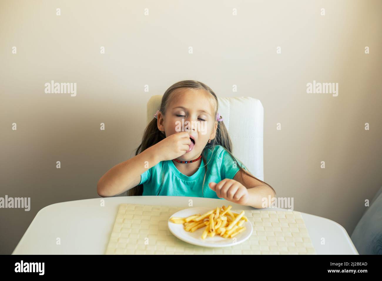 Close-up of a little girl eating French fries at the kitchen Stock Photo
