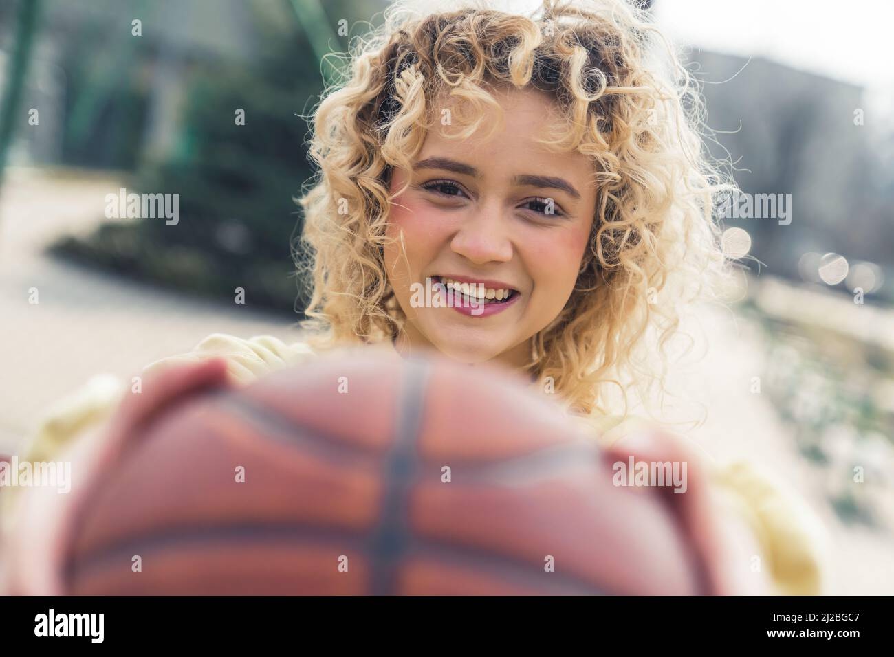 Beautiful young blond woman smiles and holds a basketball ball in front of her closeup copy space . High quality photo Stock Photo