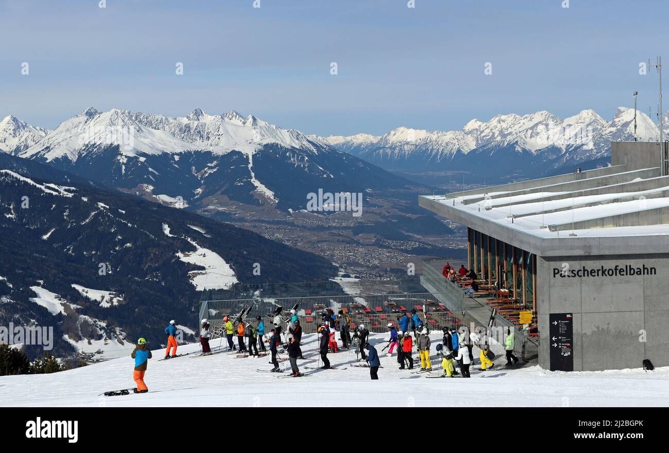 Skiers assemble outside Das Kofel restaurant at the Patscherkofelbahn's Mountain Station while the gondola rises above the Inn Valley and Innsbruck. Stock Photo