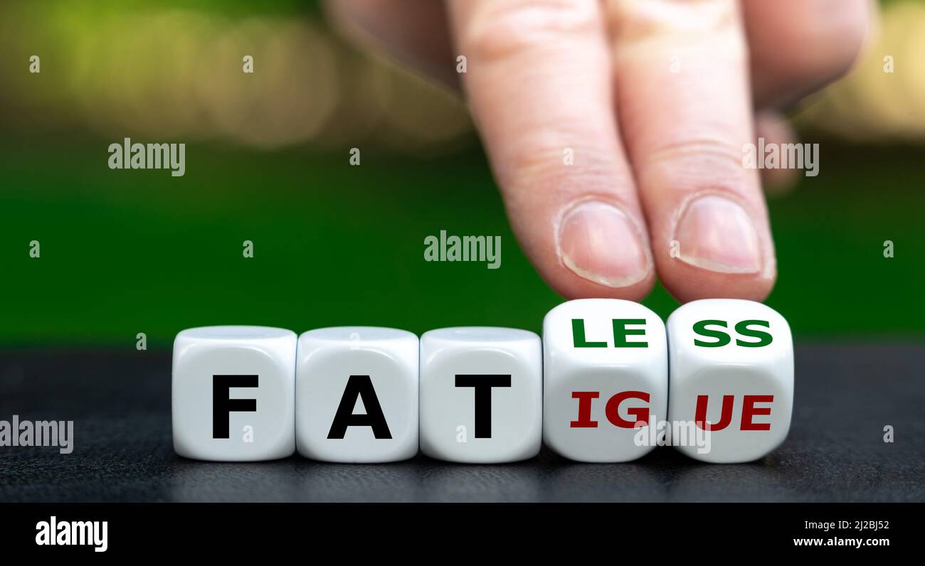 Hand turns dice and changes the word fatigue to fatless. Stock Photo