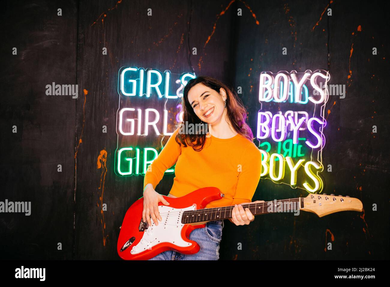 Portrait of a brunette caucasian young woman playing a red guitar, against a black background Stock Photo