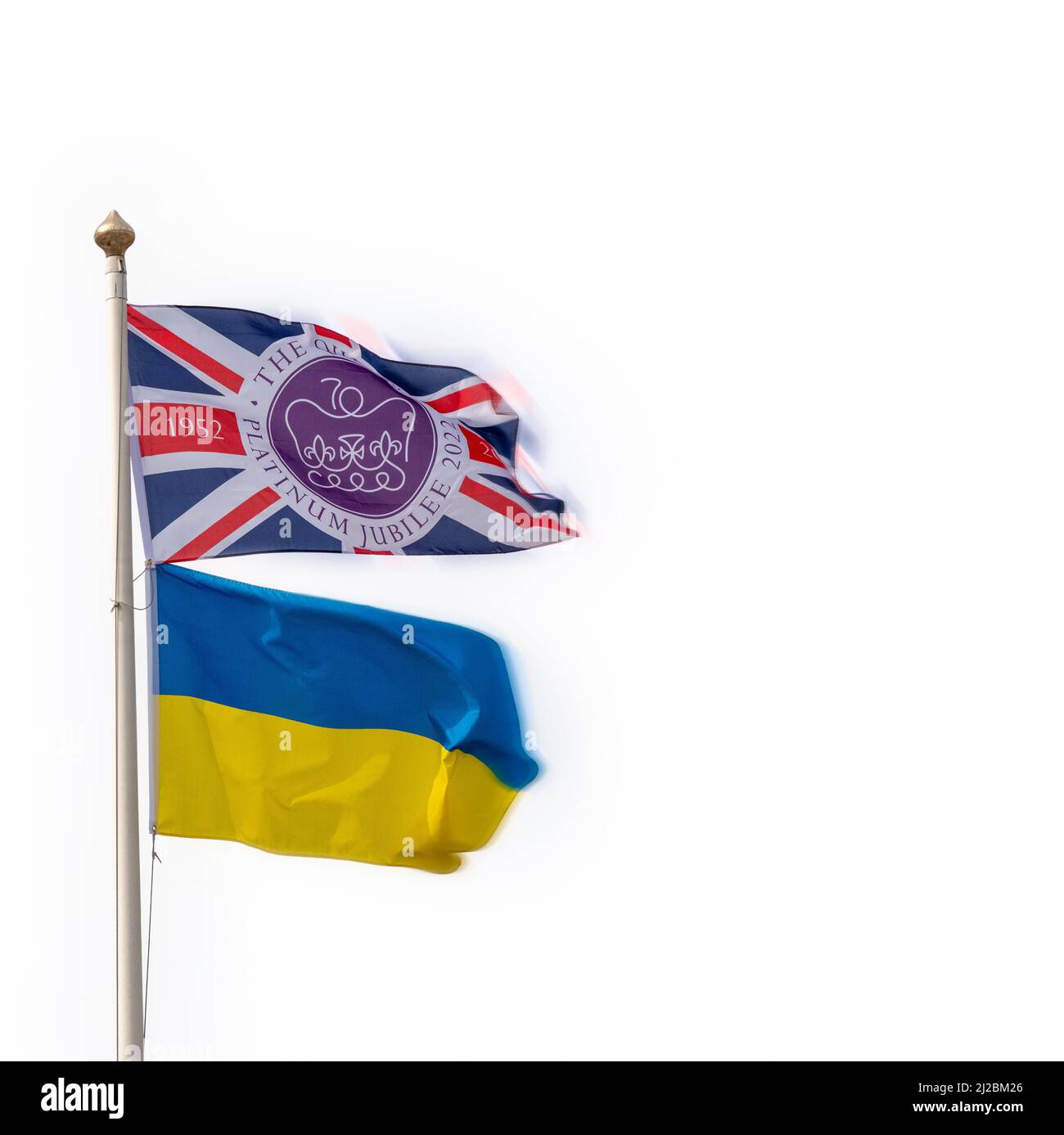 The Platinum Jubilee Union Jack flag flying on a pole along with the  Ukrainian People's Republic bicolour flag with plain pale sky behind Stock Photo