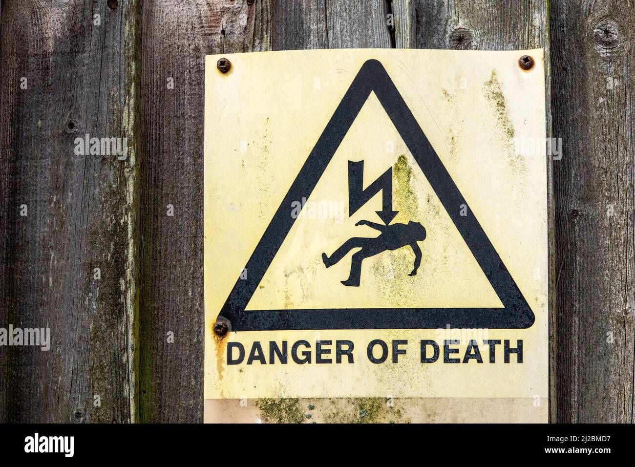 Danger of Death warning sign very faded and stained mounted on a section of heavily seasoned timber fencing Stock Photo