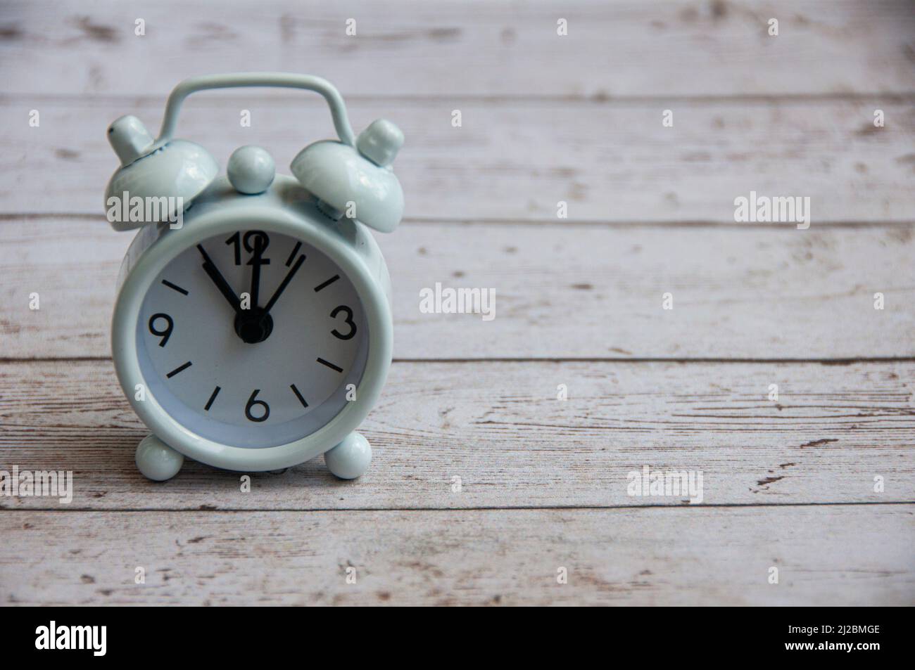 White alarm clock isolated on wooden desk. The clock set at 11 o'clock. Stock Photo