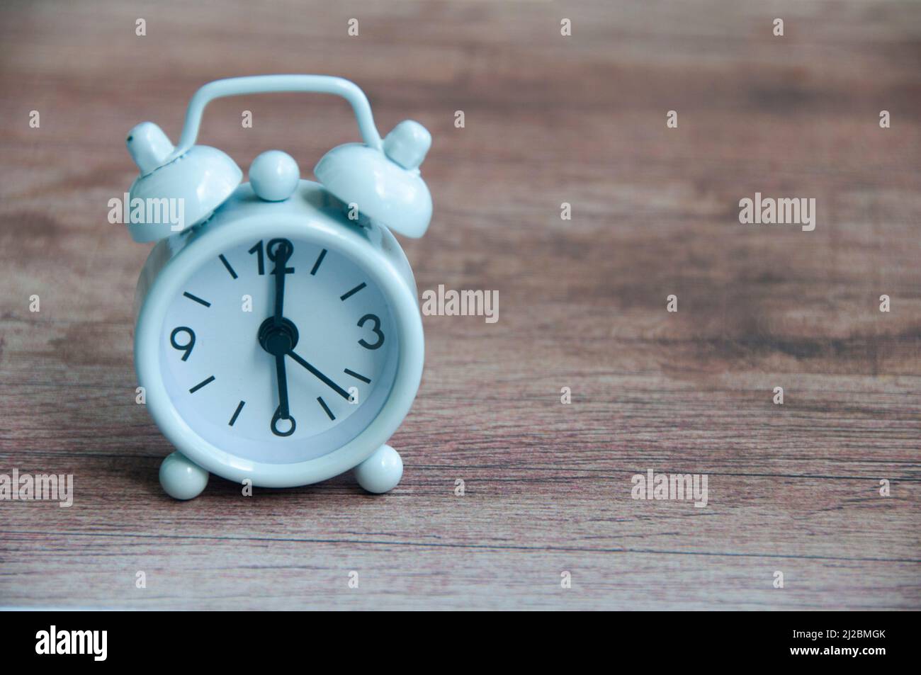 White alarm clock isolated on wooden desk. The clock set at 6 o'clock. Stock Photo