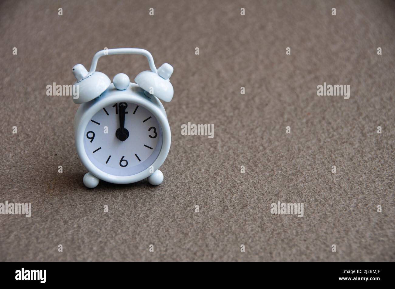 White alarm clock isolated on marble floor The clock set at 12 o'clock. Stock Photo