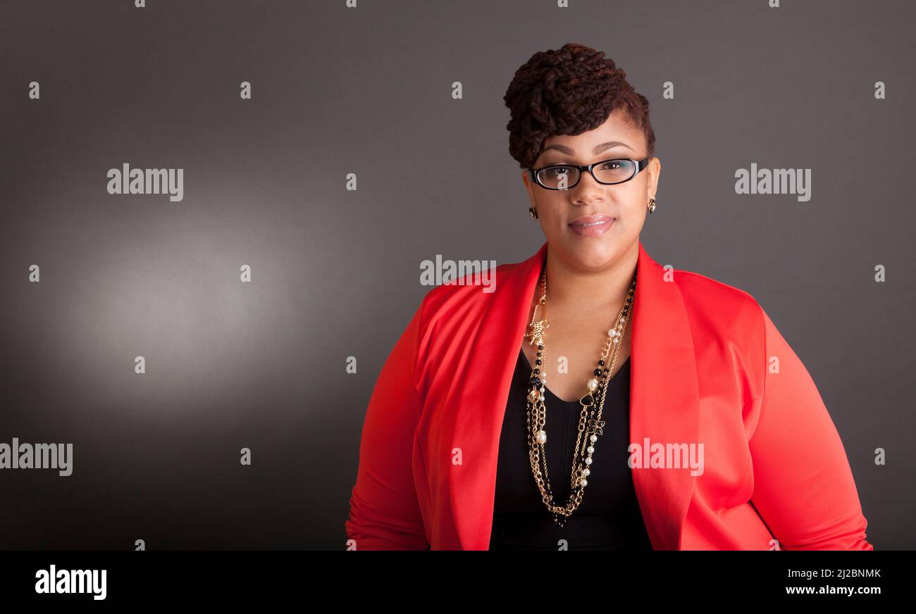 Plus size black woman wearing glasses in a smart business outfit on a neutral grey background Stock Photo