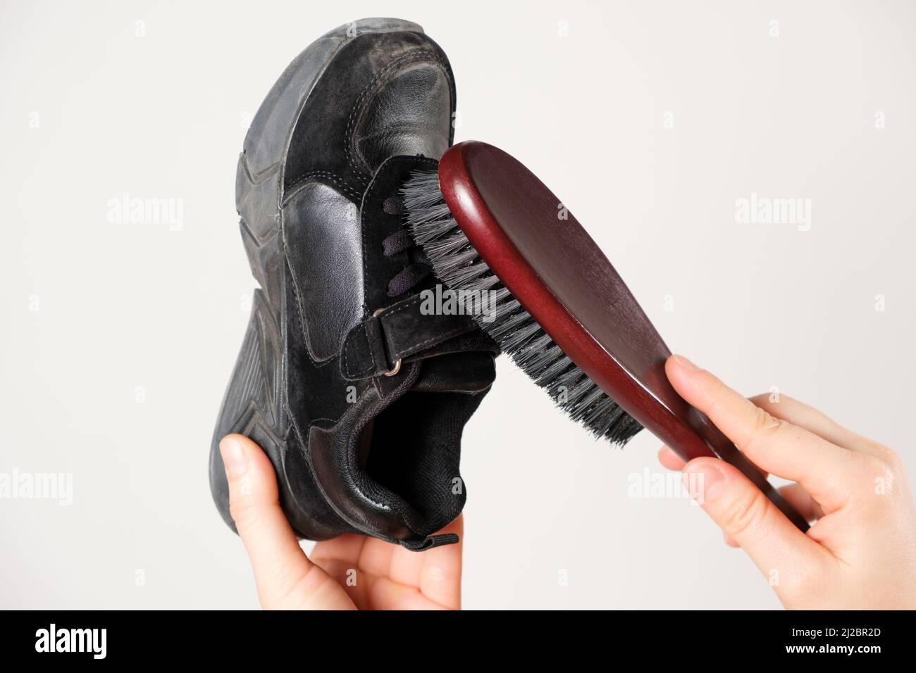A person cleans children's black sprinkles from dust with a wooden shoe brush on a white background. Care for leather and suede shoes Stock Photo