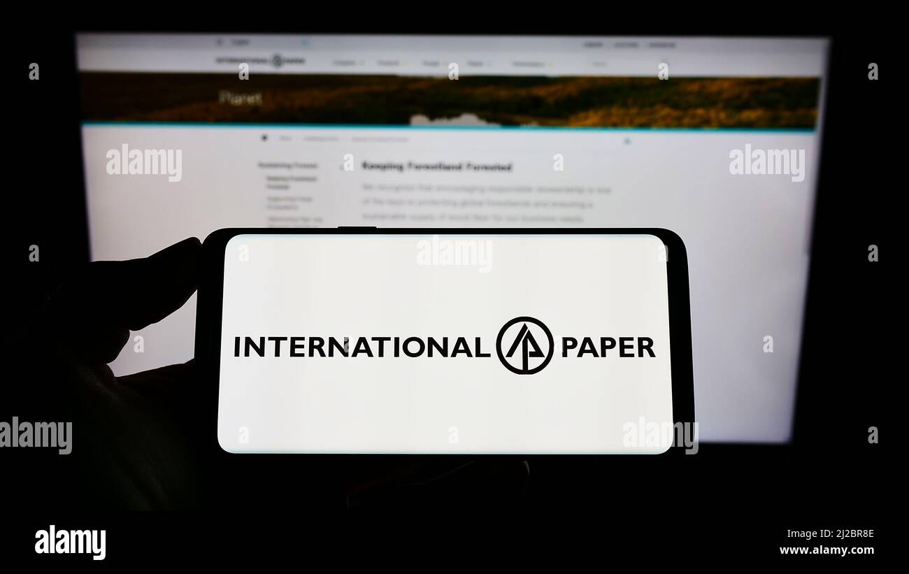 Person holding smartphone with logo of US company International Paper Company (IP) on screen in front of website. Focus on phone display. Stock Photo