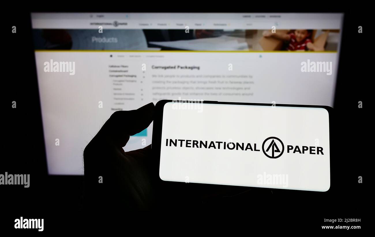 Person holding cellphone with logo of American company International Paper Company (IP) on screen in front of webpage. Focus on phone display. Stock Photo