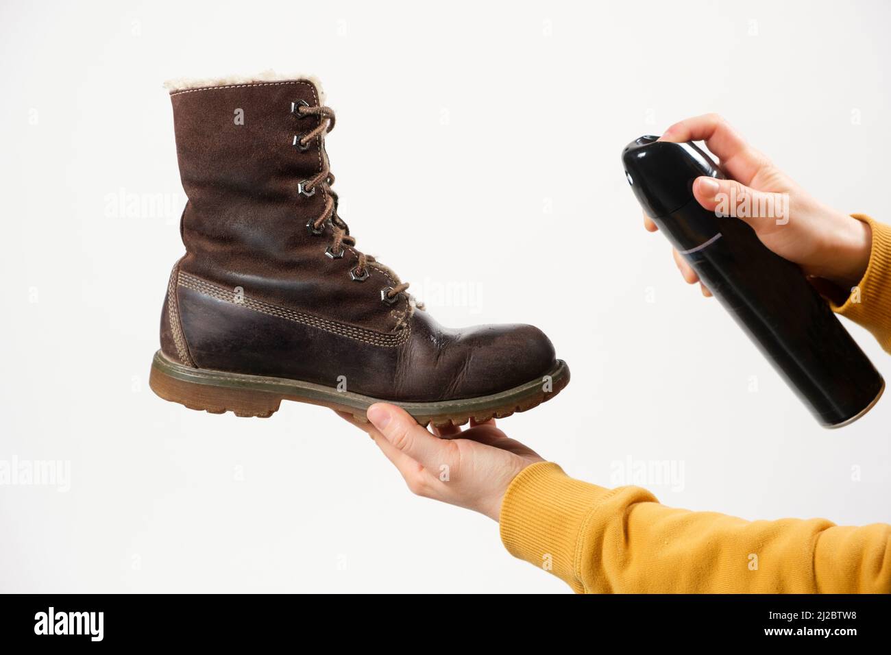 A woman applies the spray to brown nubuck women's winter boots. Water-repellent care for shoes, renewal and preservation of color Stock Photo