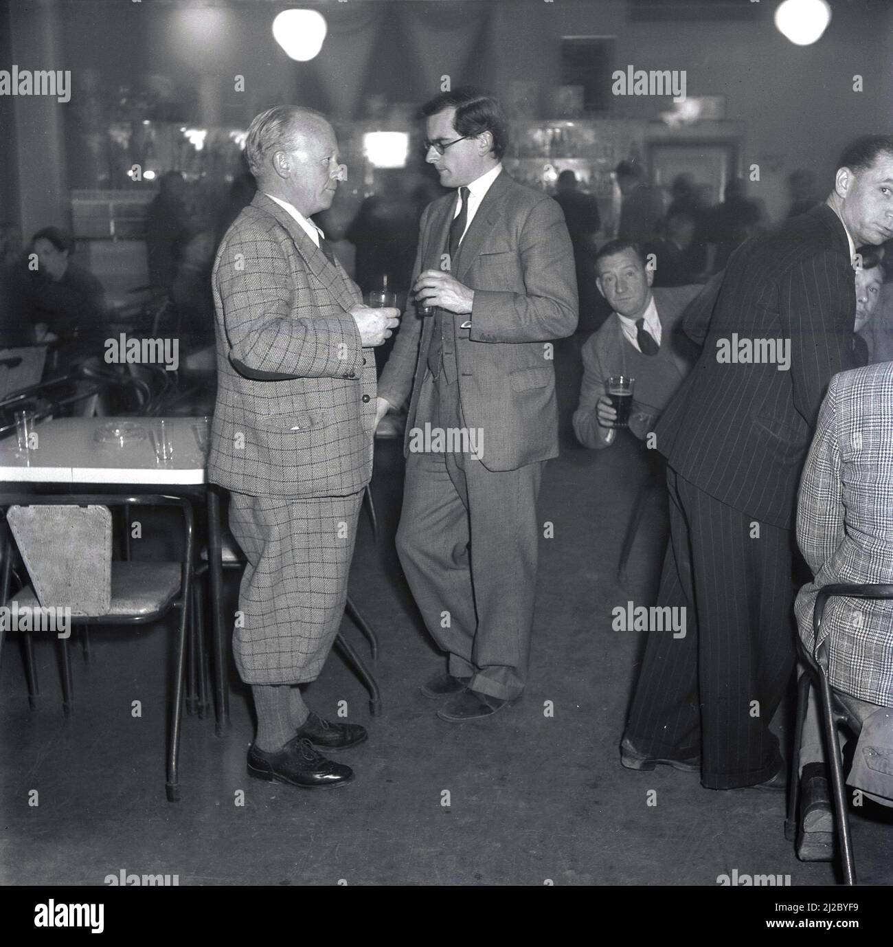1950s, historical, at a company social club, employees enjoy an evening function with colleagues. Two smartly dressed gentleman in conversation, one in a traditional suit and tie, the other, older man, wearing a check suit with plus four trousers or breeches. Post WW2 saw the formation of the The Steel Company of Wales as a public company with a mission to modernise steel production in South Wales and the site at Port Talbot/Margam was redeveloped. Abbey Works as it was named, became in the late 1950s and 60s, the biggest producer of steel in Europe and Port Talbot was the 'city of steel'. Stock Photo