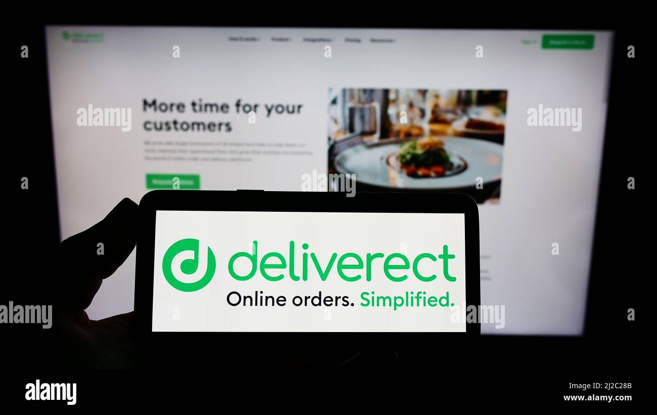 Person holding smartphone with logo of Belgian foodtech company Deliverect NV on screen in front of website. Focus on phone display. Stock Photo