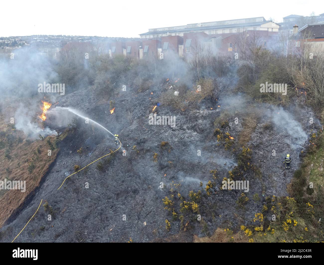 Cork, Ireland, 31st March 2022. Cork City Fire Brigade Deals with a Large Gorse Fire Near Houses in the Glen Park, Cork, Ireland. Aerial photo of members of the Cork City Fire Brigade dealing with another large gorse fire burning close to houses in the Glen River Park which runs between the Glen and Ballyvolane. Shortly after 6 pm this evening Cork City Fire Brigade attended the scene of a large gorse fire burning close to houses in Glen River Park, the smoke from this fire blew directly into the houses in the Glen area above Glen Park. A number of firefighters could be seen attending th Stock Photo