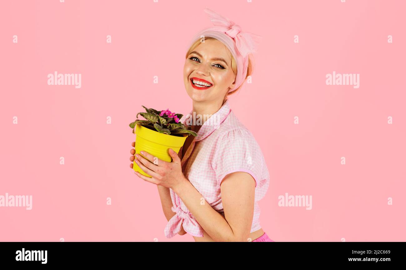 Smiling girl with blossoming African violet flower saintpaulia in pot. Woman cultivating flowers. Stock Photo