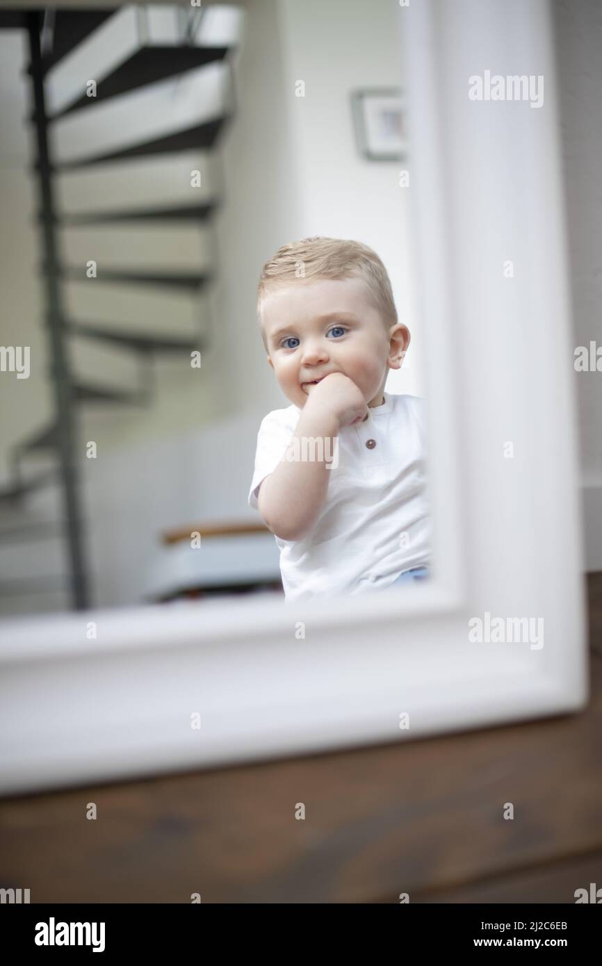 An adorable Caucasian baby boy looking in a mirror in a playroom Stock
