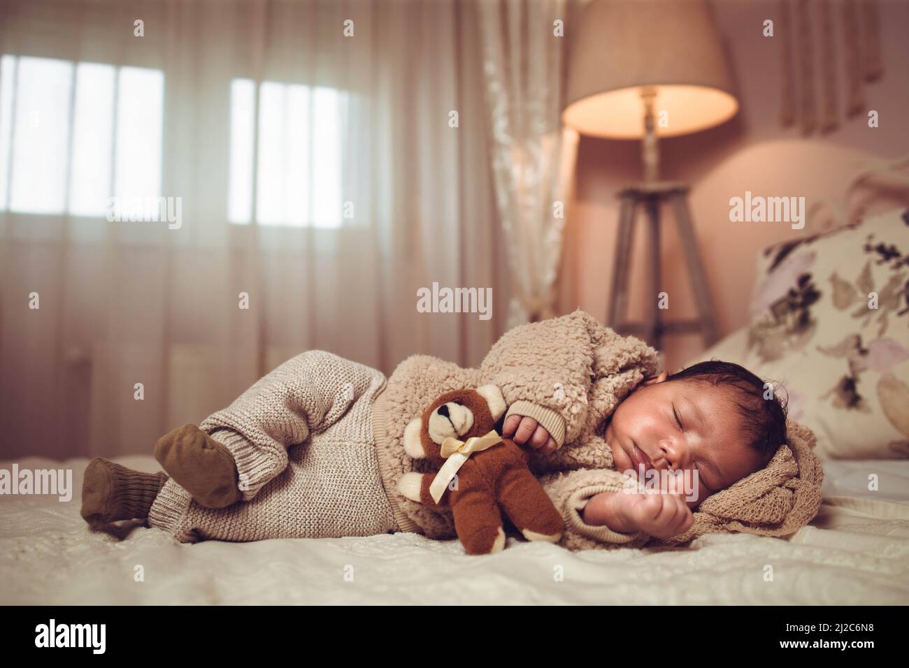 Infant multiethnic baby boy sleeping on a bed. Looking cozy with teddy bear Stock Photo