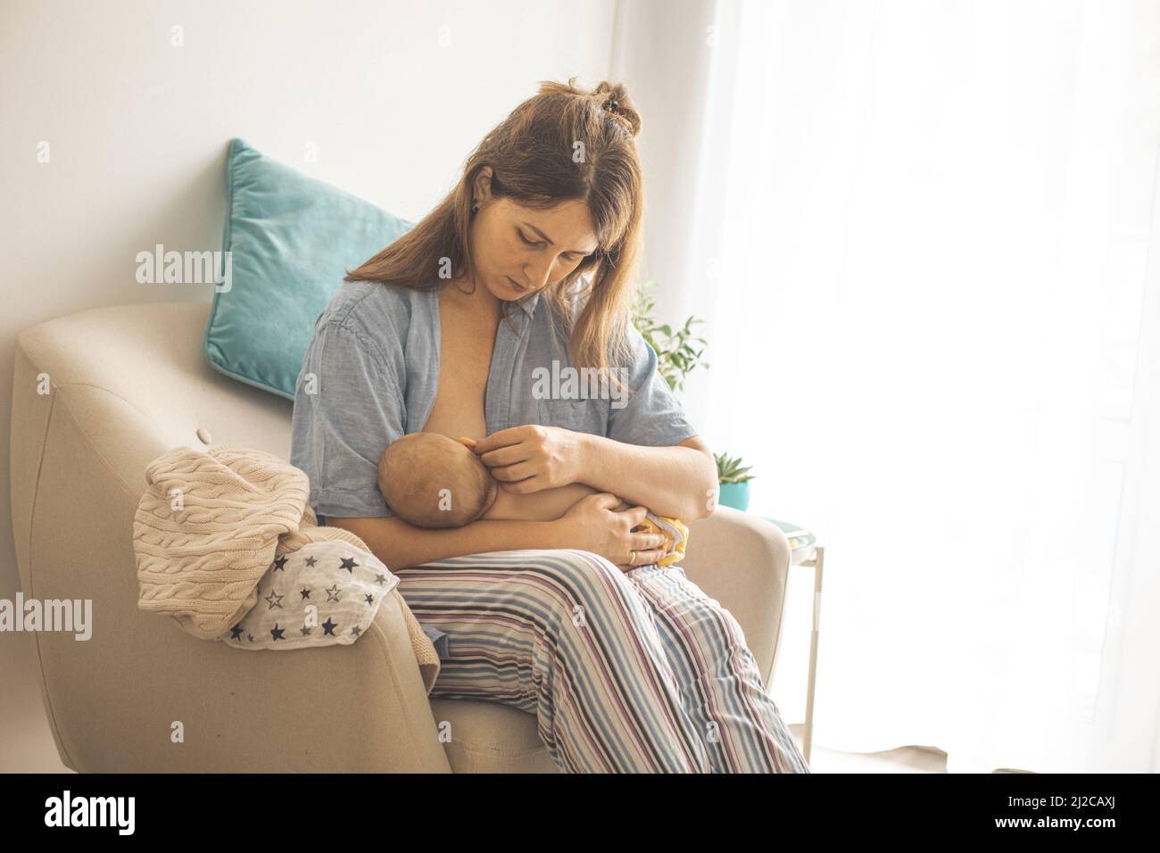 Portrait of tired and unsmiling mother breastfeeding newborn baby. Baby blues after birth. Young mother in depression. Stock Photo