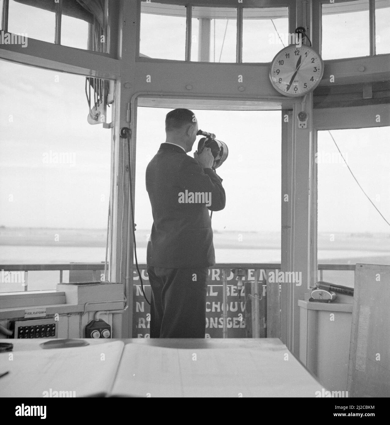 An air traffic controller in the control tower of Schiphol airport while maintaining contact with a signal lamp  ca: 1936 Stock Photo
