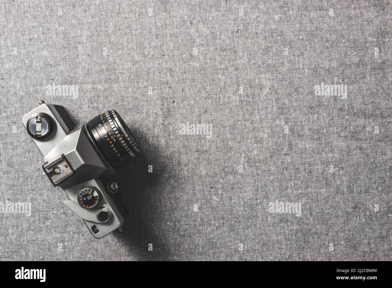 Retro analogue camera. Vintage old fashioned camera with lens on gray canvas. Top view. Stock Photo