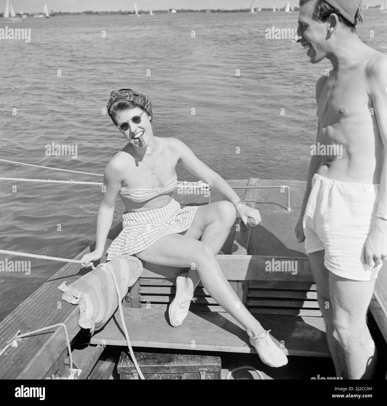 Woman in bikini with cigar in mouth, sitting at the helm next to a standing man  ca: 1946 Stock Photo