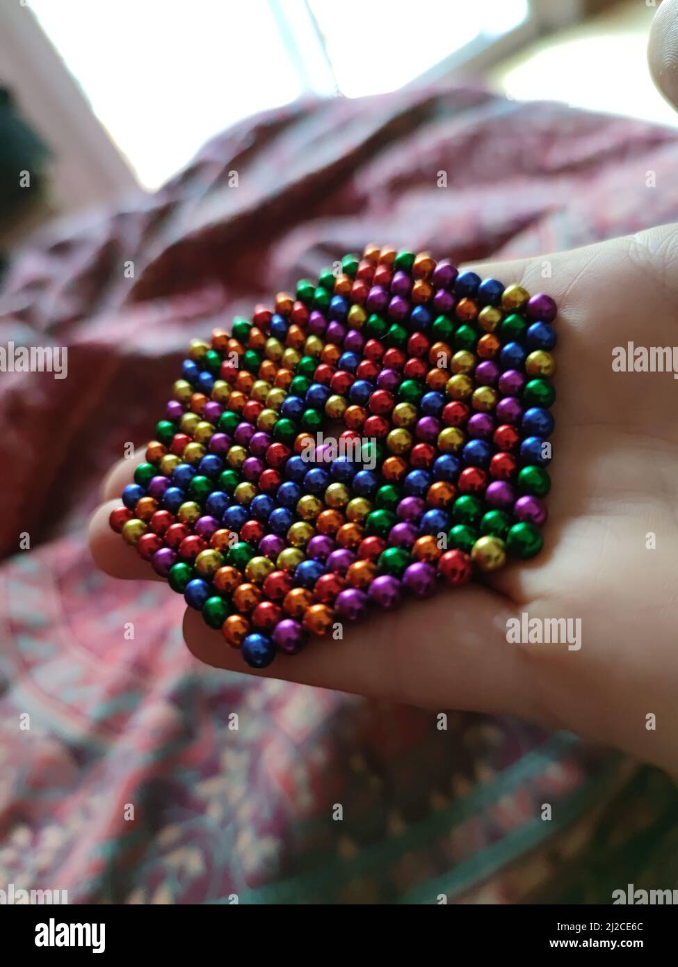 A vertical closeup of a rainbow magnetic balls stuck to each other in a  person's hand Stock Photo - Alamy