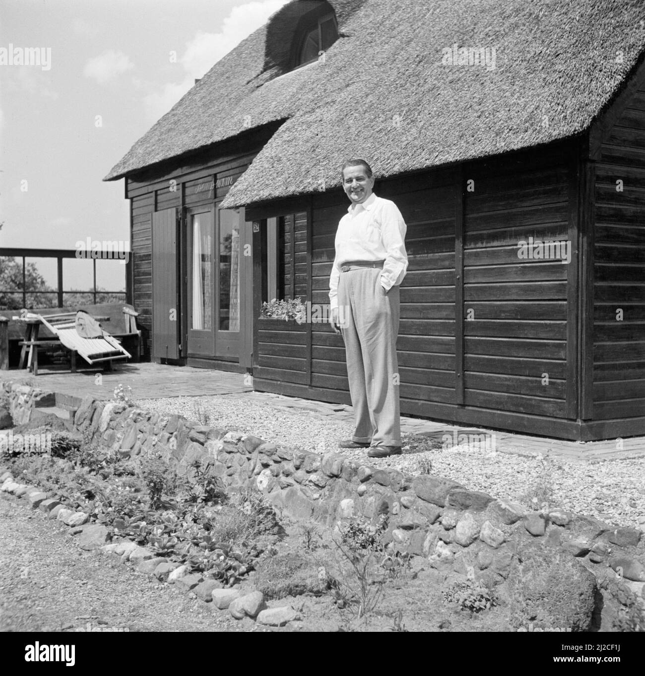 The conductor Eduard van Beinum stands smiling with one hand in his pocket at his country house Bergsham in Garderen ca: June 5, 1954 Stock Photo