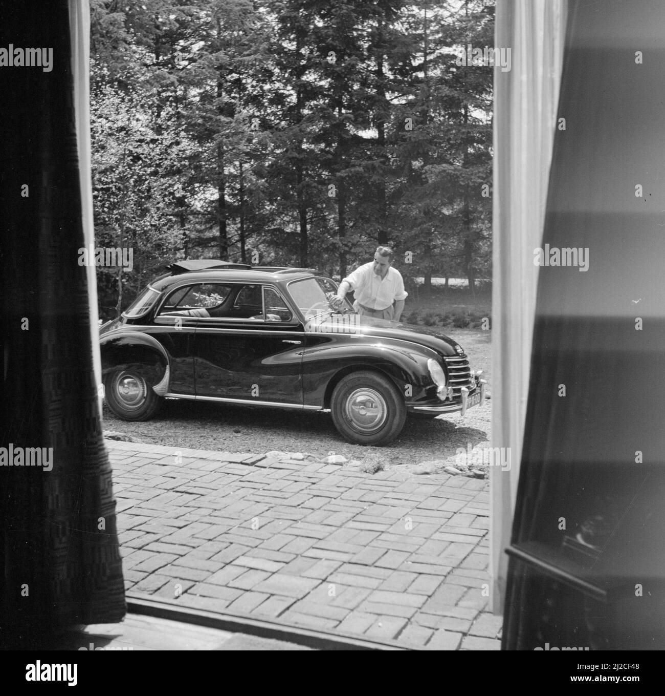 The conductor Eduard van Beinum washes the windscreen of his open DKW at his country house Bergsham in Garderen ca: June 5, 1954 Stock Photo