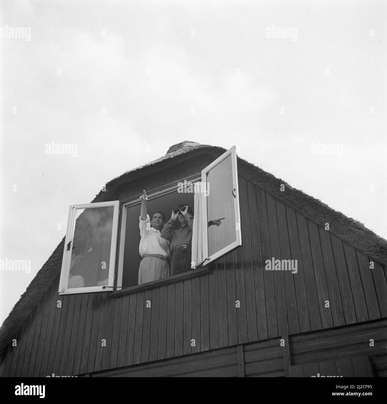 The conductor Eduard van Beinum points his son Bart, with binoculars, to something in the distance from an open window of their Bergsham country house in Garderen. ca: June 5, 1954 Stock Photo