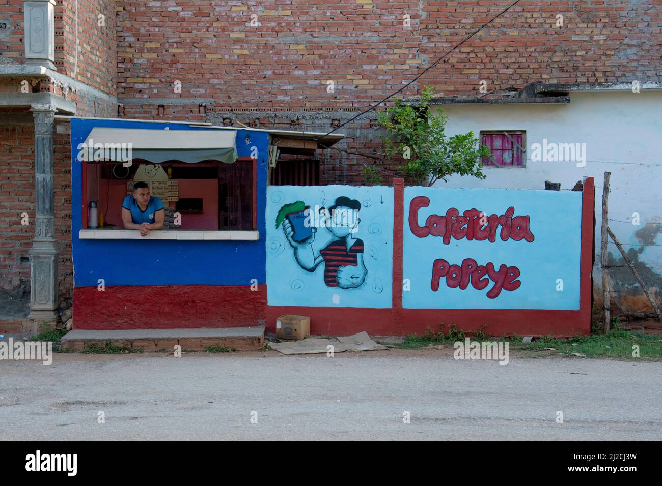 Cuban worked leans on the table of a mural drawing of Popeye the sailor man at a cafe on a street in Trinidad, Cuba. Stock Photo