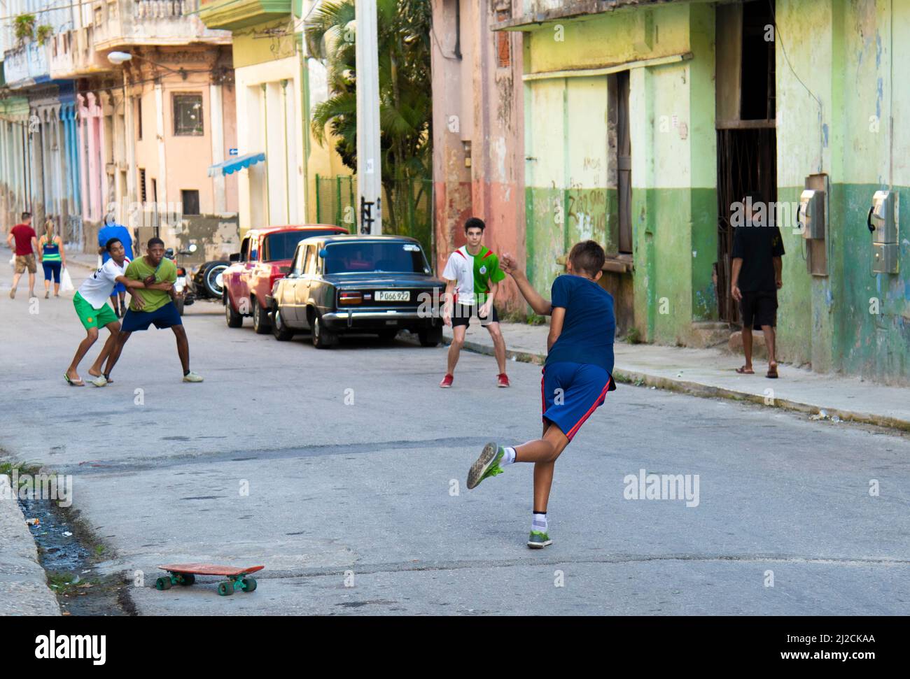 Young man hits and plays with a tennis ball and his friends on a street in Havana, Cuba in front of a skate board on the street. Stock Photo