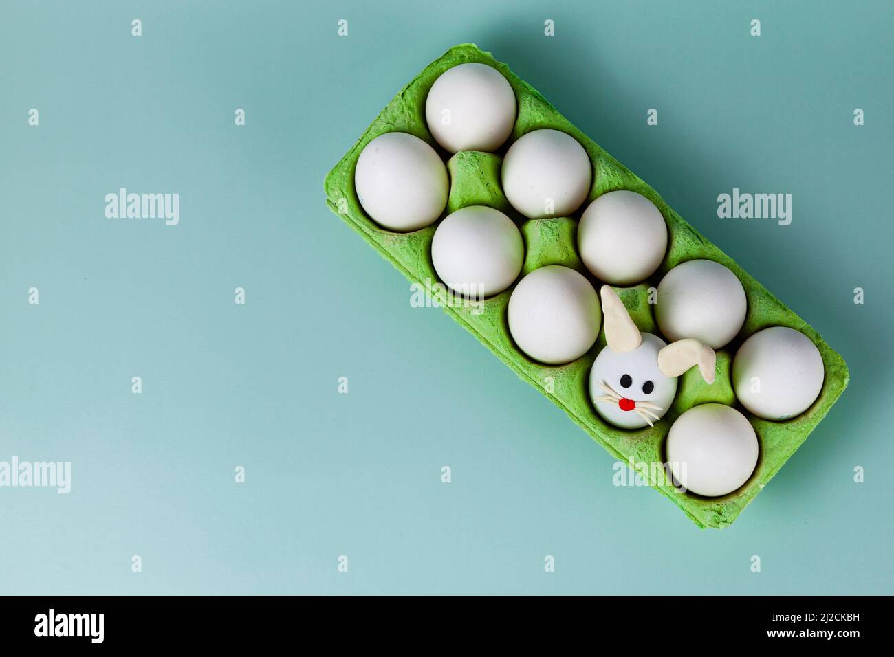Happy Easter. Easter eggs. Chicken white eggs on green background. One egg with easter bunny ears. Closeup. Stock Photo
