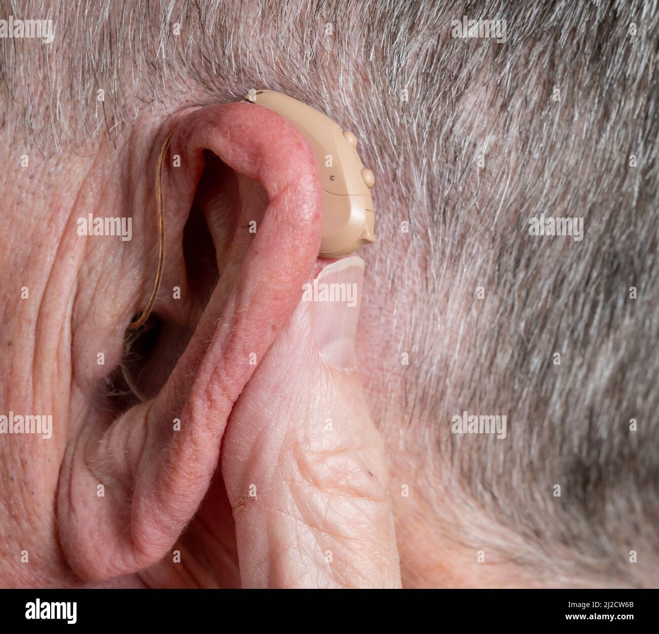 Macro close up of tiny modern hearing aid placed behind the ear of senior adult man Stock Photo