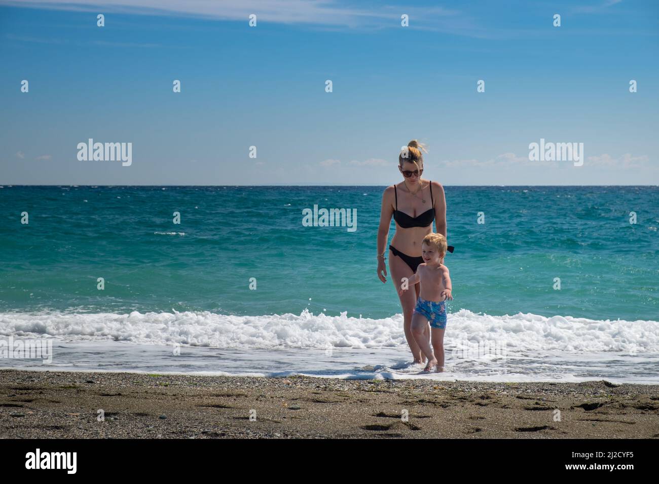 summer happy family of two years blonde baby with blue swimsuit walking in  water ocean holding hand with woman mother bikini in Stock Photo - Alamy