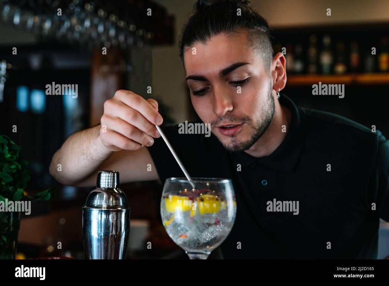 Young bartender stirring a mixed drink in a crystal glass with a slice of citrus fruit and ice. Stock Photo