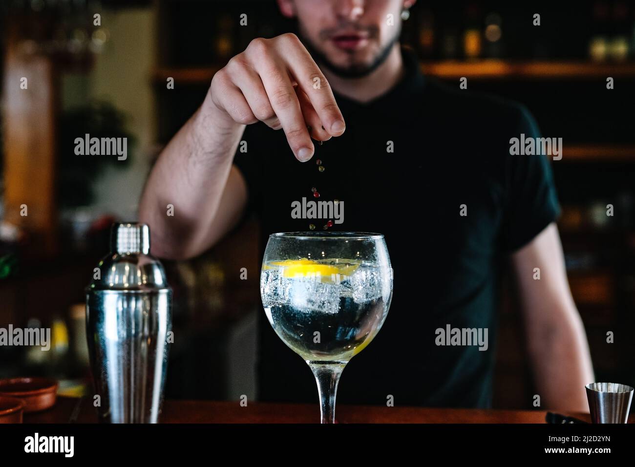 Detail of a bartender's hands adding ingredients into a crystal glass with ice for mixed drinks. Nightclub. Stock Photo