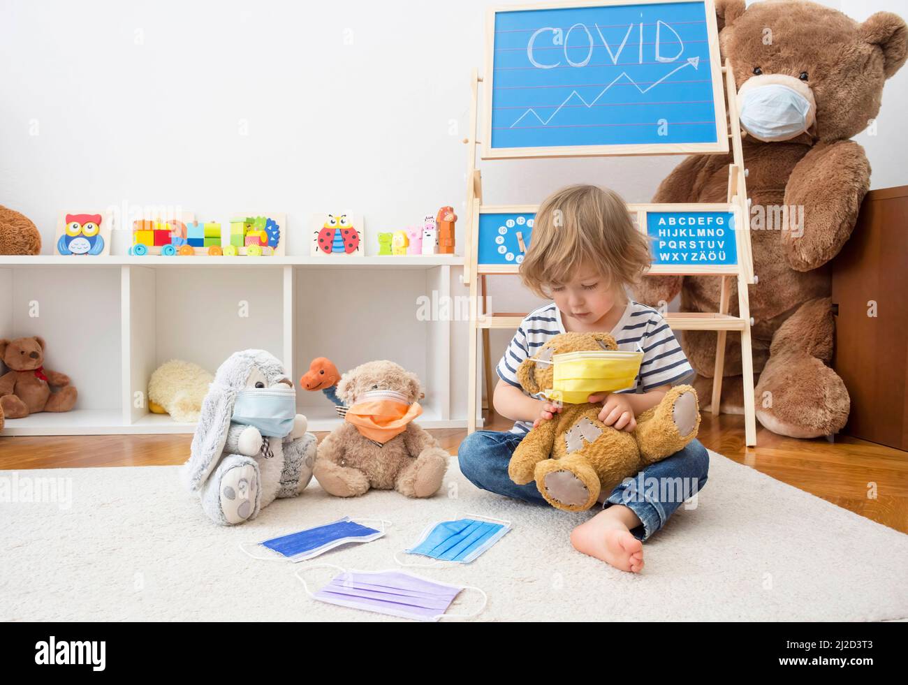 Cute child boy in home quarantine playing doctor on the floor with his sick teddy bears wearing medical masks during coronavirus COVID-2019 and flu ou Stock Photo