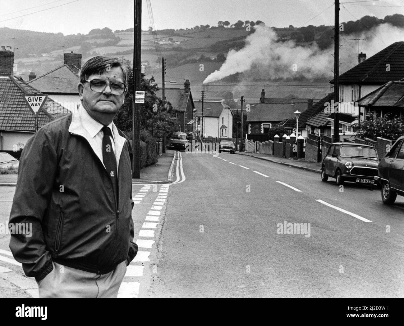 An everyday scene in Risca, Mr John Herbert pictured in Gelli Avenue with the smoke billowing from the Brickhouse Dudley factory chimney. Valley residents face a year-long wait before £500,000 worth of clean air equipment is fitted at the foundry after a row over pollution. 22nd August 1986. Stock Photo