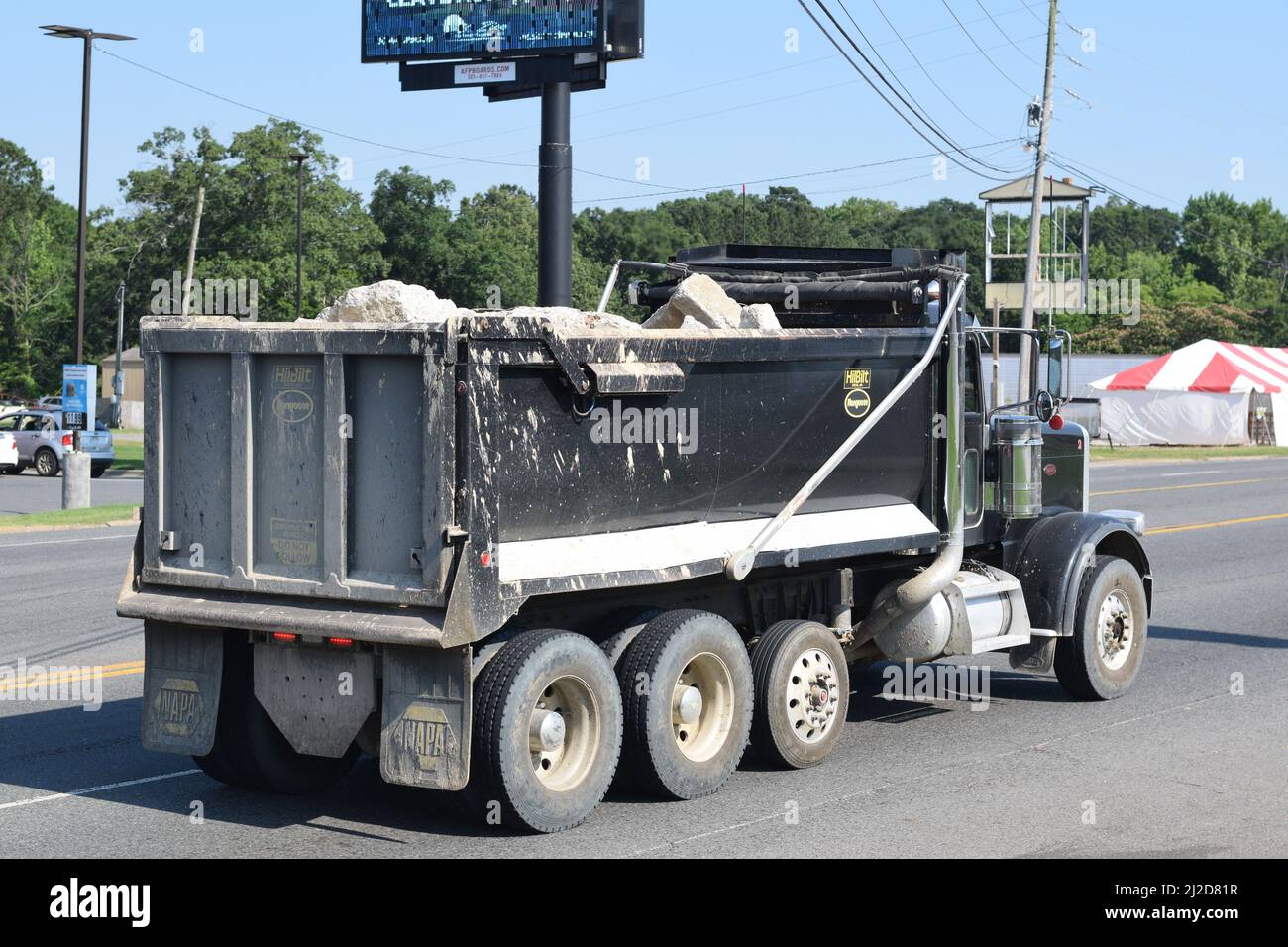 Black dump truck filled with broken slabs of concrete driving on a four