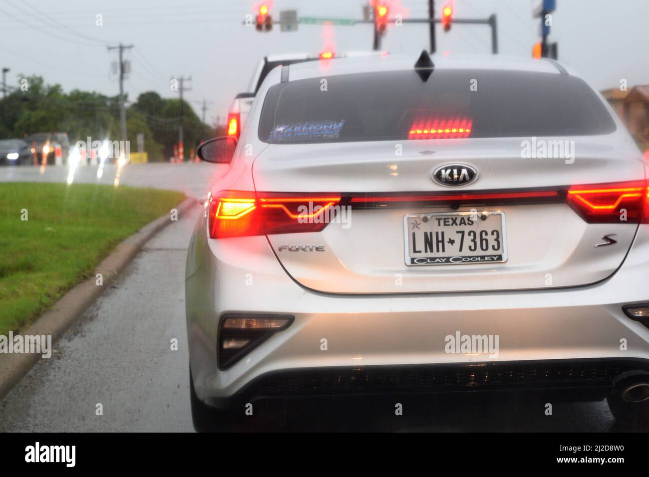 A white car with brake lights on stopped at a traffic light on a rainy